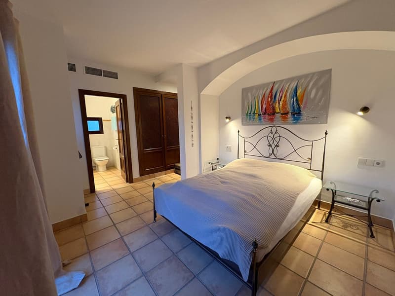 bedroom with bed, tile floor, closet, bedside tables, wall art, en-suite bathroom with toilet
