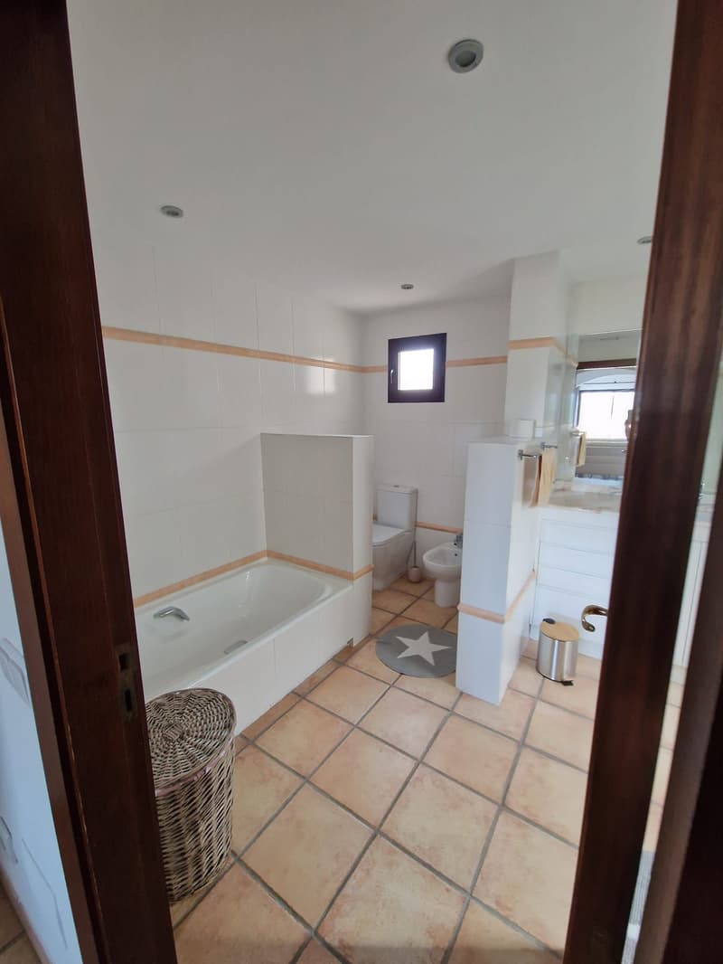Bathroom with bathtub, bidet, toilet, sink, mirror, tiled floor, wicker basket, trash bin, towel rack.