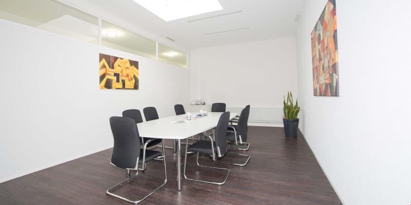 conference room with white walls, wooden floor, long white table, black chairs, two paintings, potted plant