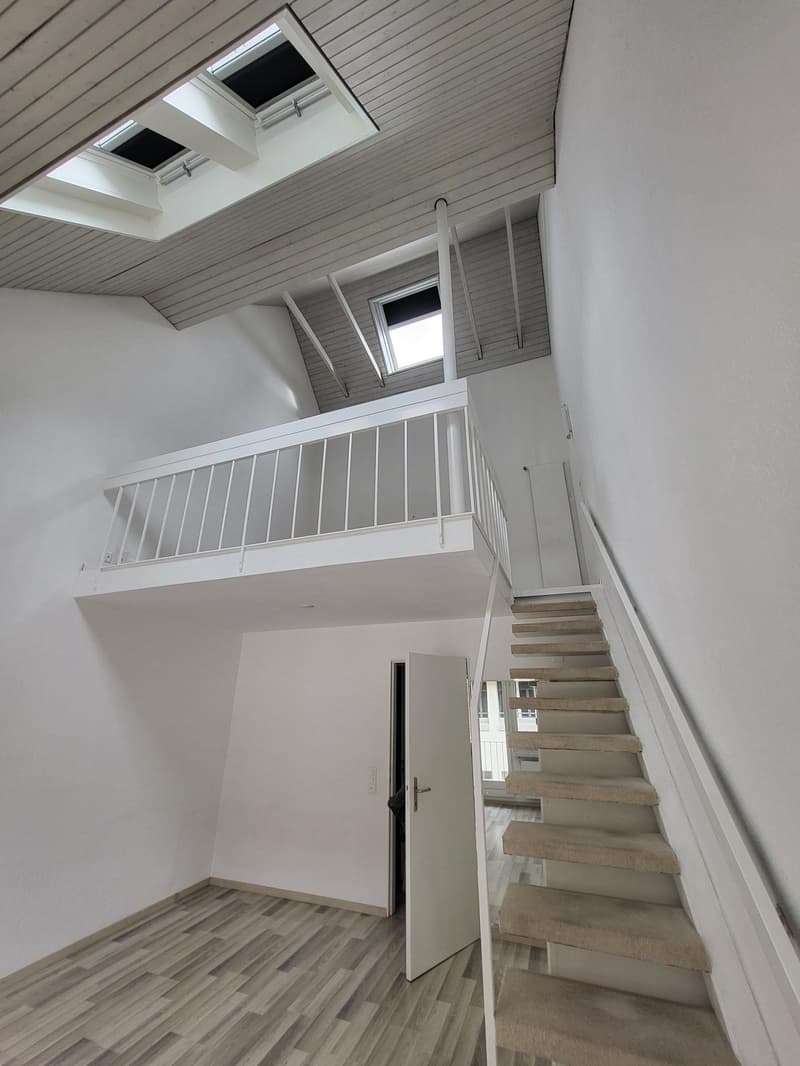 loft style interior with exposed wooden beams, white walls, open staircase leading to upper floor, balcony