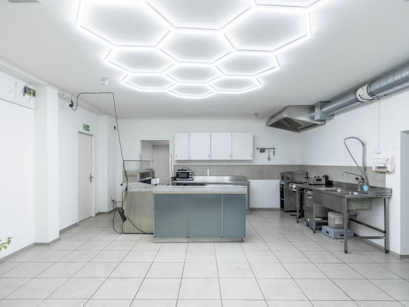 Open kitchen with modern design, white cabinets, white tiled floor, stainless steel countertops, built-in appliances, large hexagonal light fixture, kitchen island with appliances and countertop
