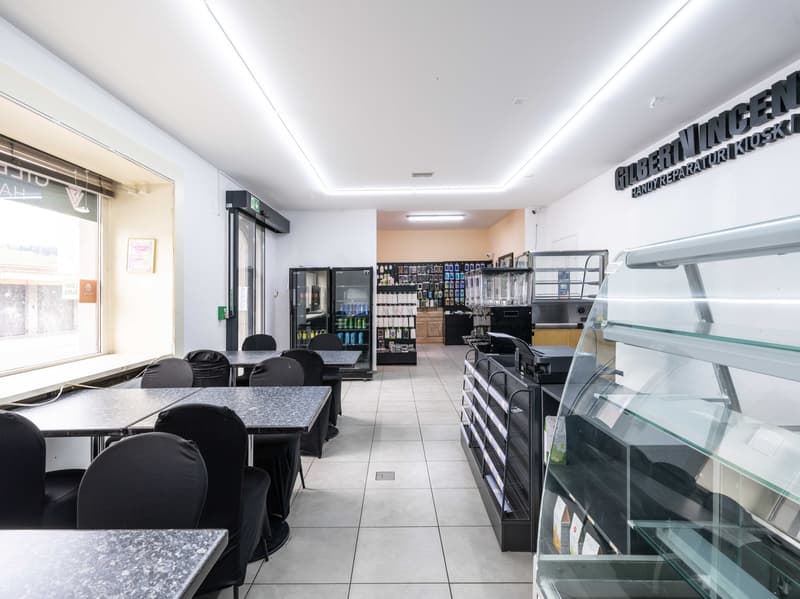 Commercial space with black tables and chairs, tiled floor, glass display case, fridges, and vending machines.