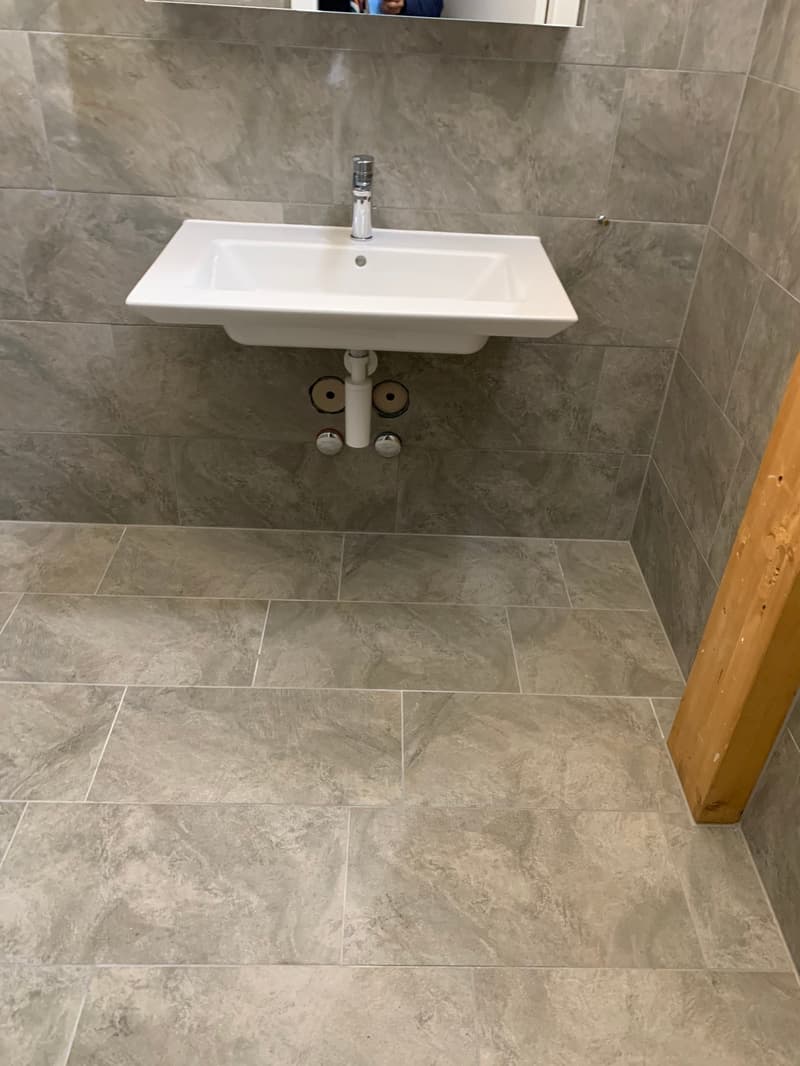 A simple bathroom with a square sink, gray tiles, and a mirror on the wall.