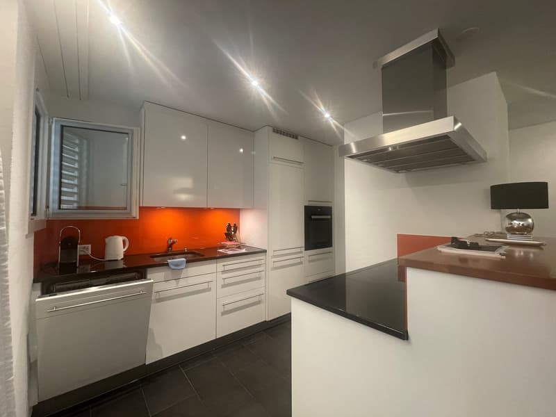 Modern, open-concept kitchen with white cabinets, black countertops, built-in appliances including a dishwasher, and an orange backsplash. The kitchen has a sleek and minimalist design.