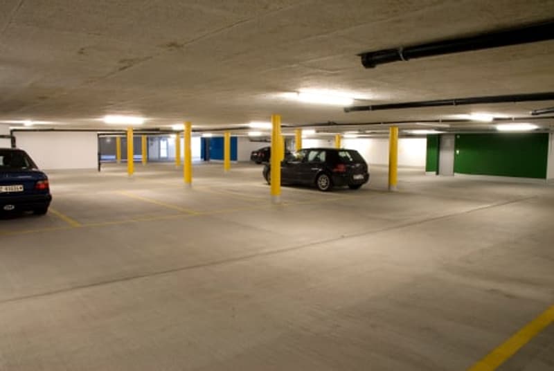 Large indoor parking garage with concrete floors, yellow and blue pillars, and several parked cars.