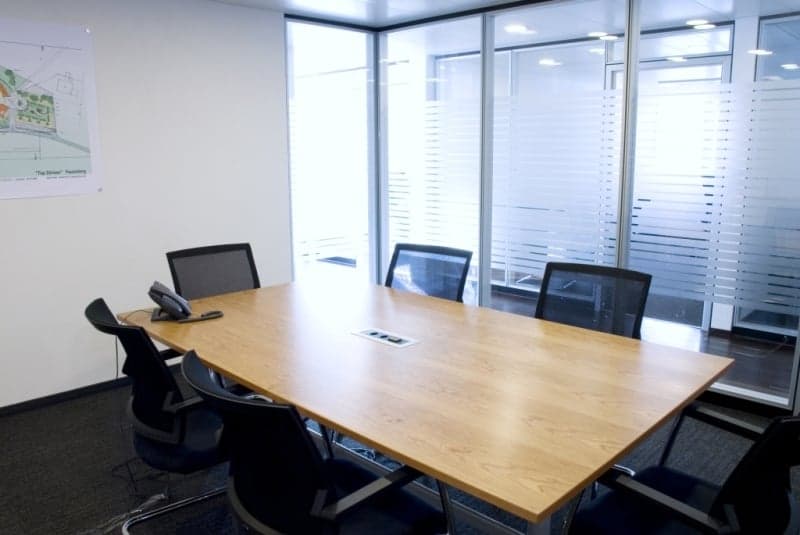 conference room with a long wooden table, black chairs, a telephone, and glass walls