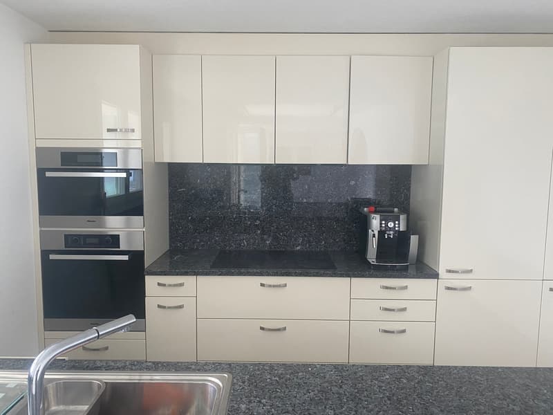 modern white cabinets, black granite countertops, stainless steel oven and dishwasher, granite backsplash, coffee machine, sink, faucet