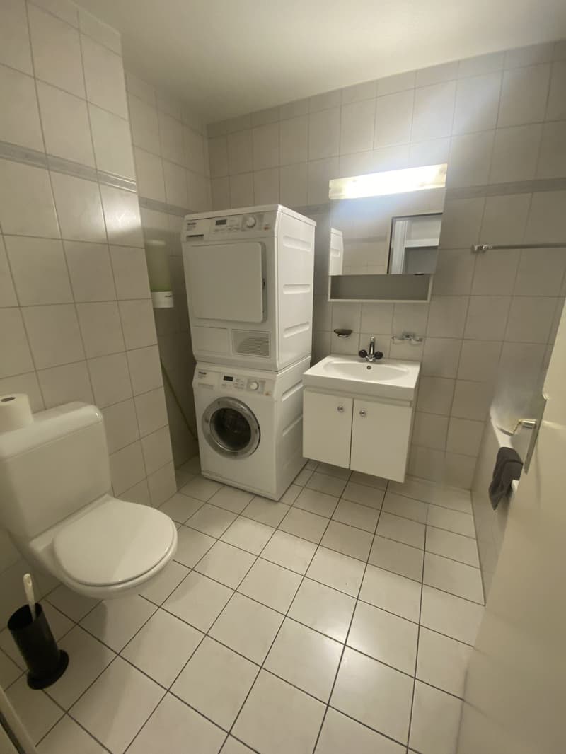 Tiled floor, white sink, white toilet, stacked washing machine and dryer, bathtub