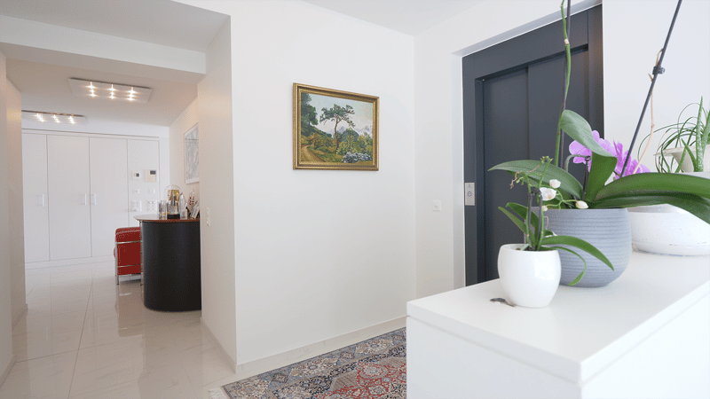 white tiled floor, white walls, ceiling lights, rug, black desk, red chair, framed painting, potted plants, gray door, storage cabinets, wall outlets