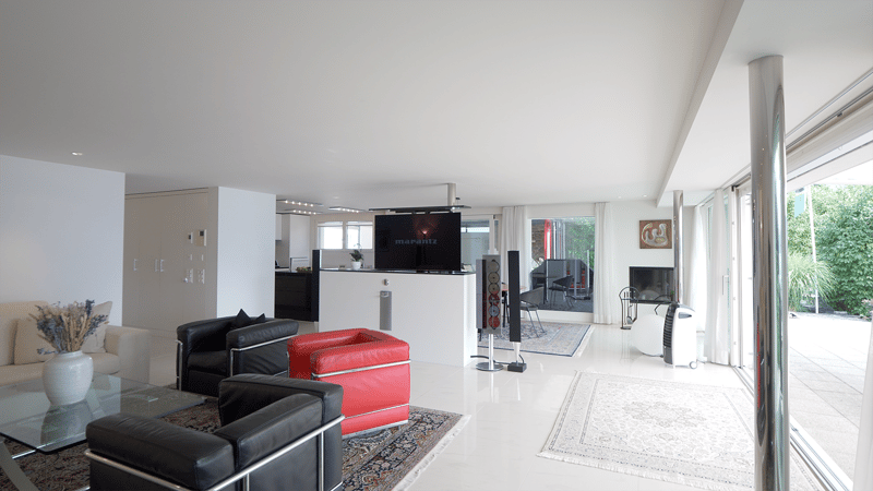 modern living room, white walls, white tiled floor, glass doors to terrace, large sofa, glass coffee table, black leather chairs, red leather armchair, flat screen TV, speakers, black fireplace, air cooler, rug