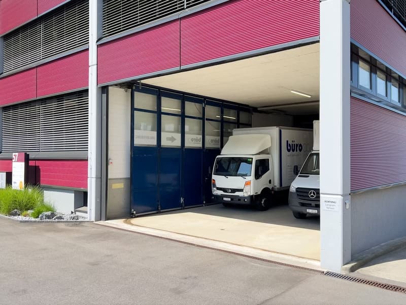 A warehouse building with two trucks parked inside, two automated doors, a red and white design, and metal panels.