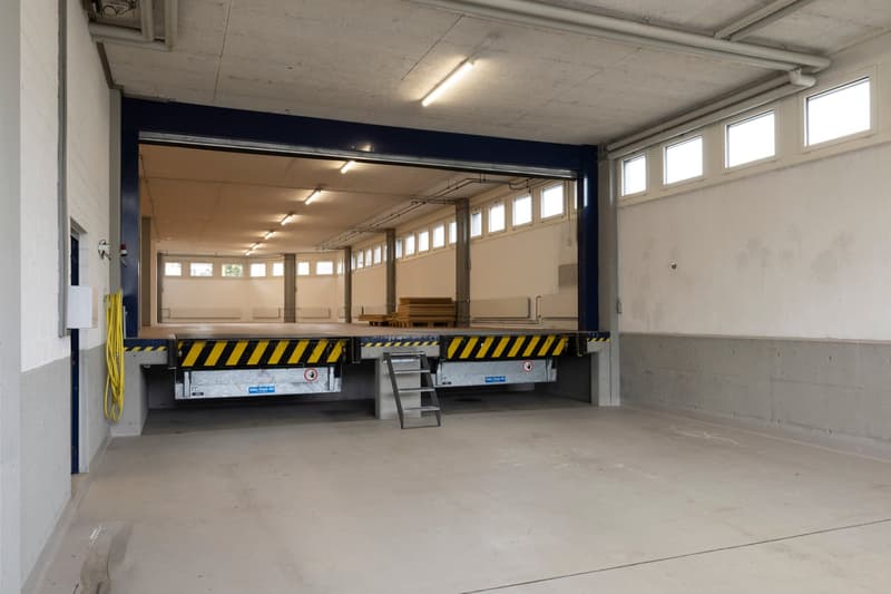 Empty garage with a lift platform, metal ladder, and yellow hose