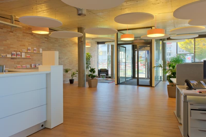 large lobby with large windows, wood floors, brick walls, hanging lamps, potted plants, office furniture, front desk
