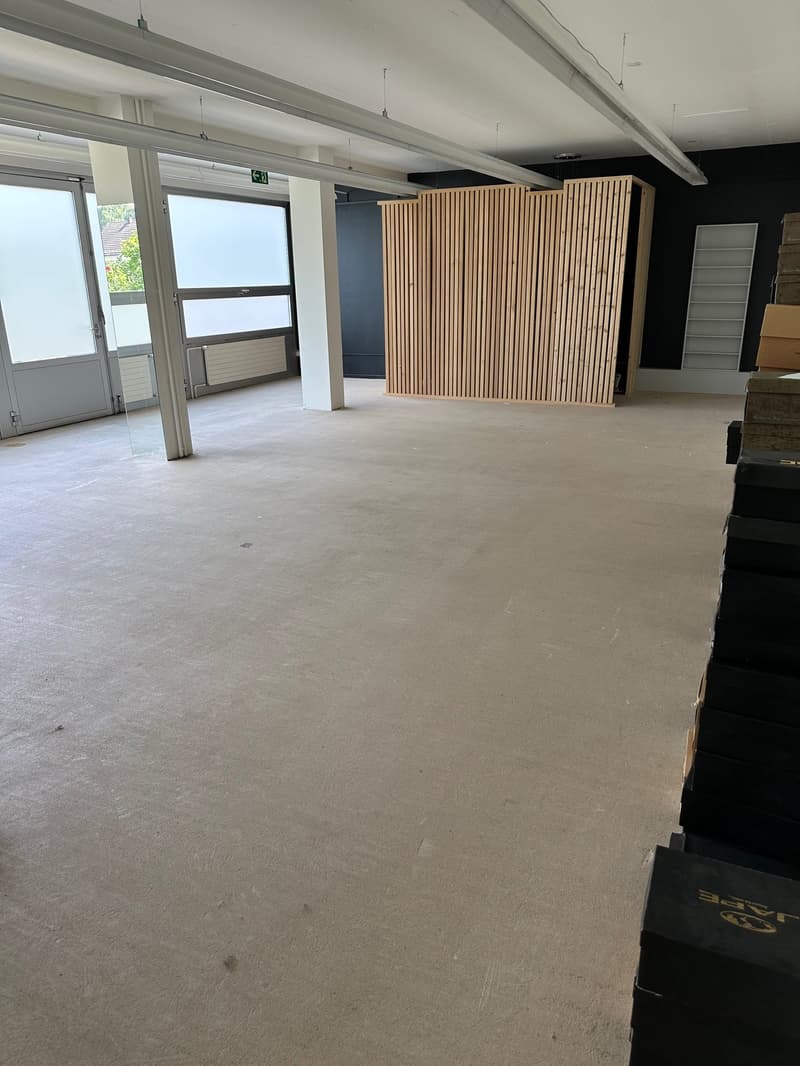 Empty room with white walls, beige floor, ceiling mounted lights, large wooden partitions, glass doors, shelves.