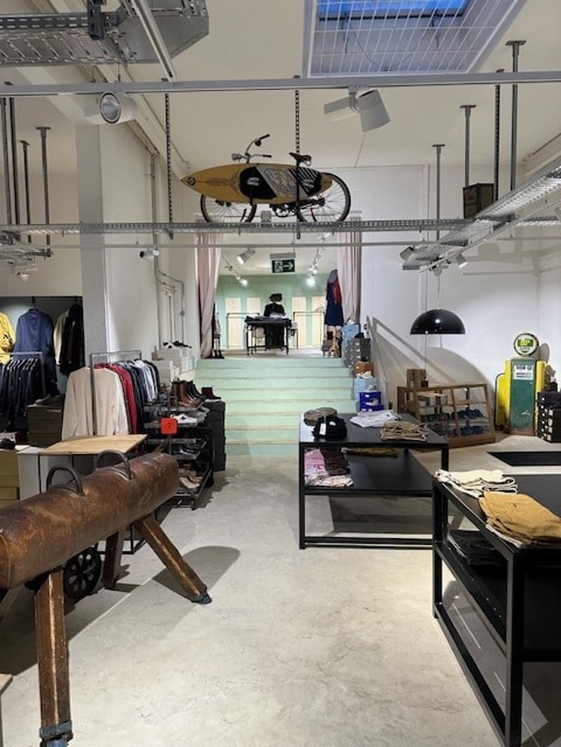 clothing store interior, clothing racks, counter, wooden shelves, bicycle hanging from ceiling, various apparel displayed