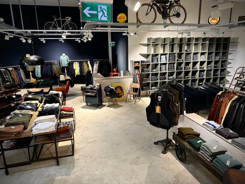 clothes on racks, wooden tables, shelves with clothes, hanging bicycles, bright lights