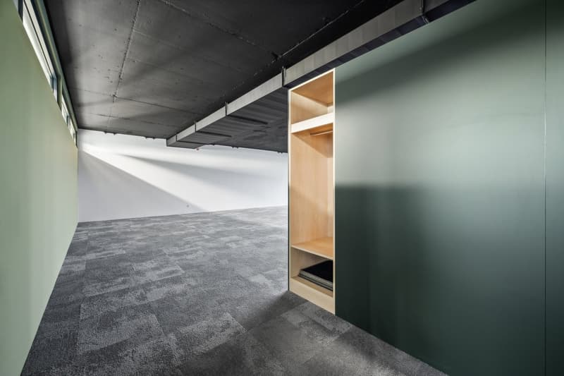 Large open space with concrete ceiling, gray carpeted floor, and built-in shelving unit