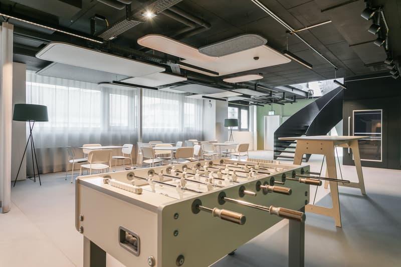 Large open office space with modern furniture, including a foosball table, and large windows providing natural light. The space has a contemporary, industrial design with exposed ceilings and lighting fixtures.