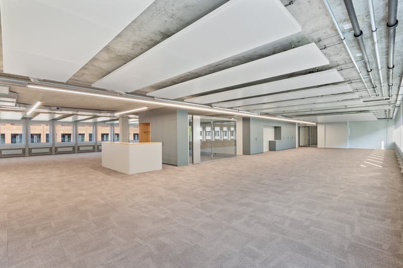 spacious room, neutral-colored carpet, large windows, modern ceiling with integrated lights, grey storage cabinets, reception desk