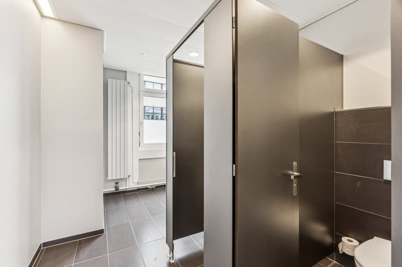 Sleek, modern bathroom with tiled floors, large mirrors, chrome fixtures, two shower stalls, and a toilet.