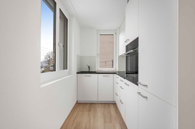 a kitchen area with white cupboards, wooden flooring, and windows