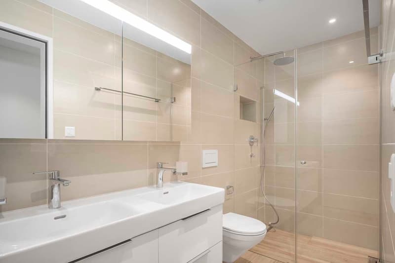 Bathroom with walk-in shower, vanity, toilet, and beige tiles.