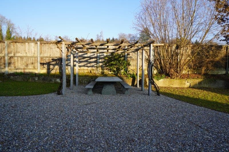 wooden pergola, concrete table, gravel surface, wooden fence