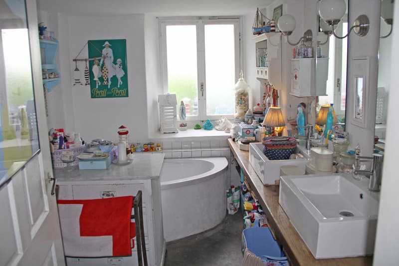 Cluttered bathroom with a round sink, various decorative items, and a dishwasher visible.