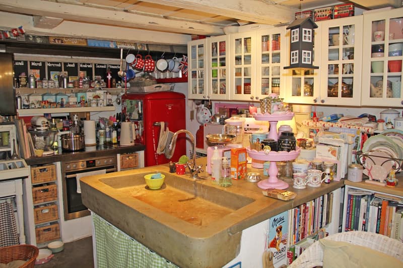 Vintage-style kitchen with a red retro refrigerator, concrete countertop, shelves filled with kitchenware and decor, and a dishwasher and washing machine visible.