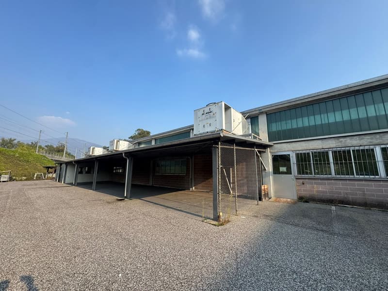 Industrial building with an open carport, three AC units on the roof, metal fence and entrance door