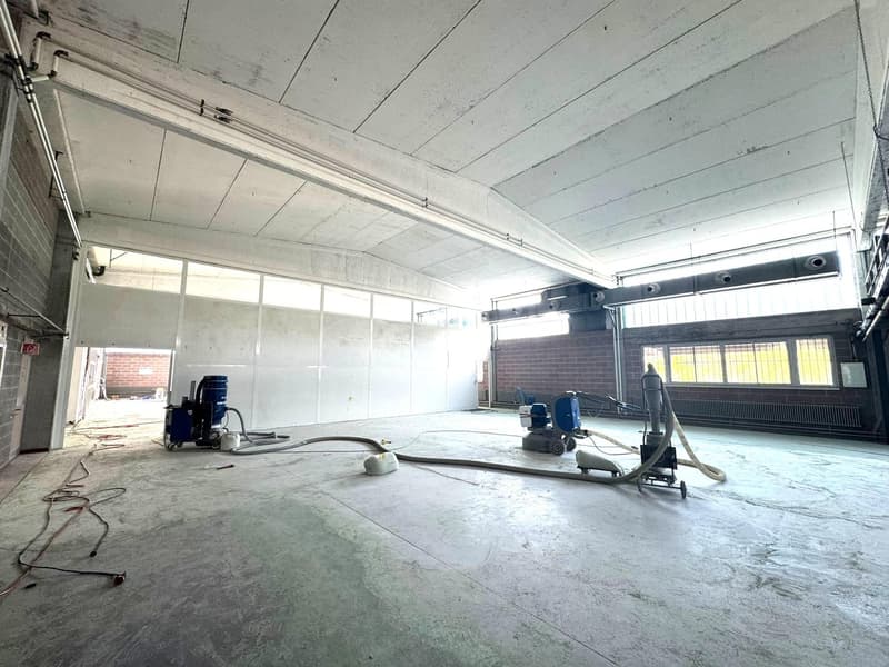 empty room with white ceiling, brick walls, large windows, some tools and pipes on the floor