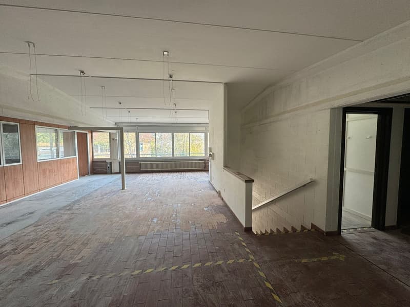 large hallway with wooden floors, glass windows, staircase with handrail, radiators, blank walls, yellow markings on the floor