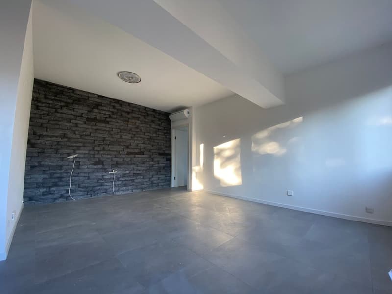 Empty room with white walls, gray tile flooring, brick wall, air conditioner, power outlets