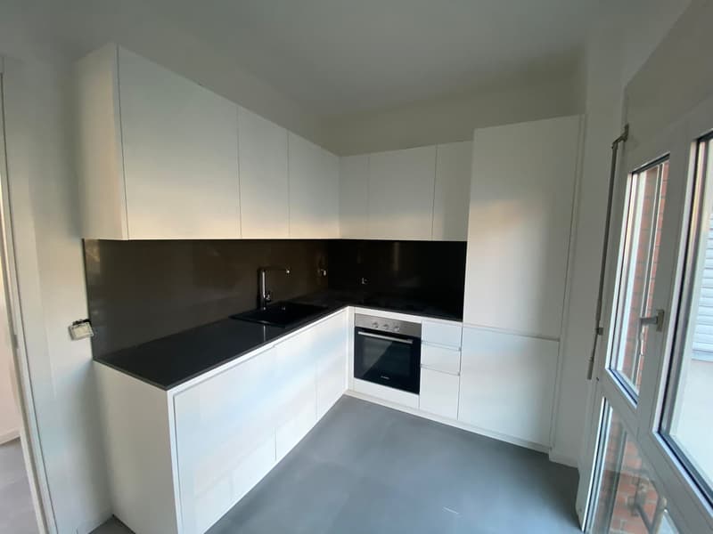 modern kitchen with white cabinetry, black countertops, stainless steel sink and faucet, built-in oven and dishwasher, and a sliding glass door leading to an outdoor area