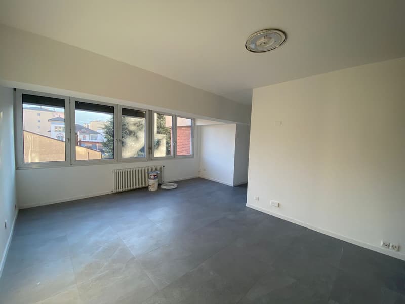 Large empty room, tiled floor, large windows, white walls, ceiling light