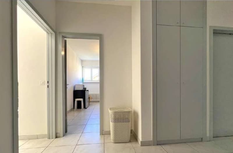 Empty hallway with tile flooring, closets, a trash bin, an open door, and a table with a printer on top.