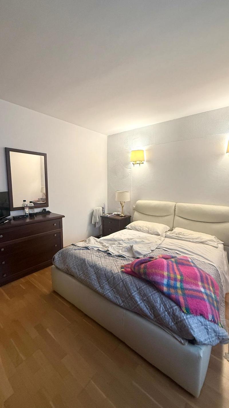 wooden floor, white bed with blankets, large mirror, dark colored dresser, bedside lamps, bedside table