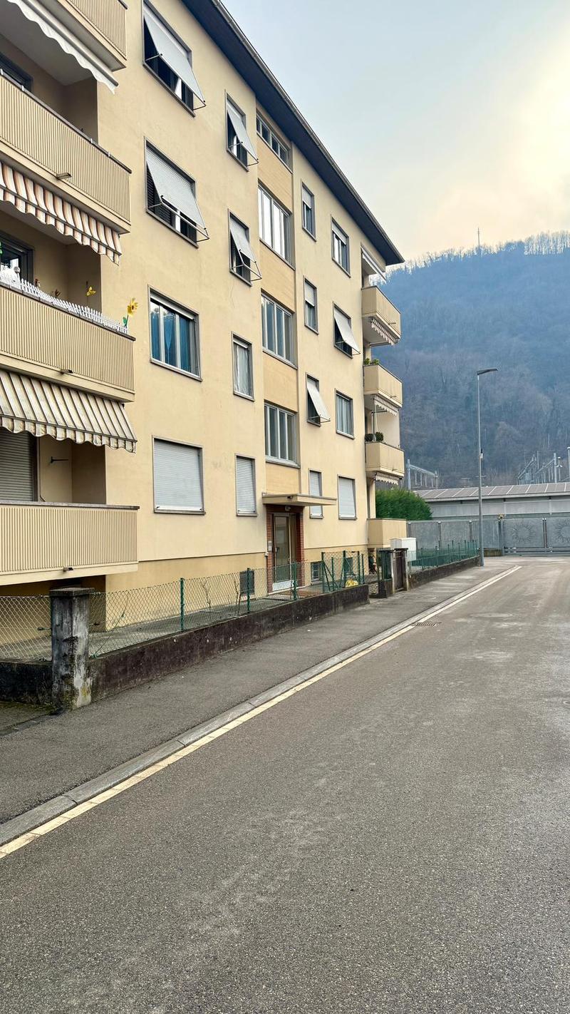 Apartment building with multiple floors, balconies, awnings, fenced entrance, street view.