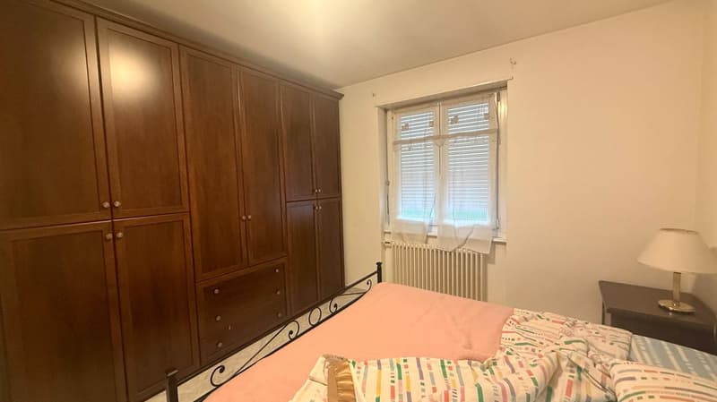 Built-in wardrobes, large bed, night stand, lamp, radiator, window with curtains and shutters