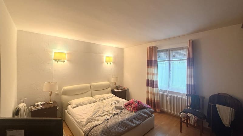 bedroom with bed, nightstands, lamps, window with curtains, radiator, wooden chair, chair with clothes