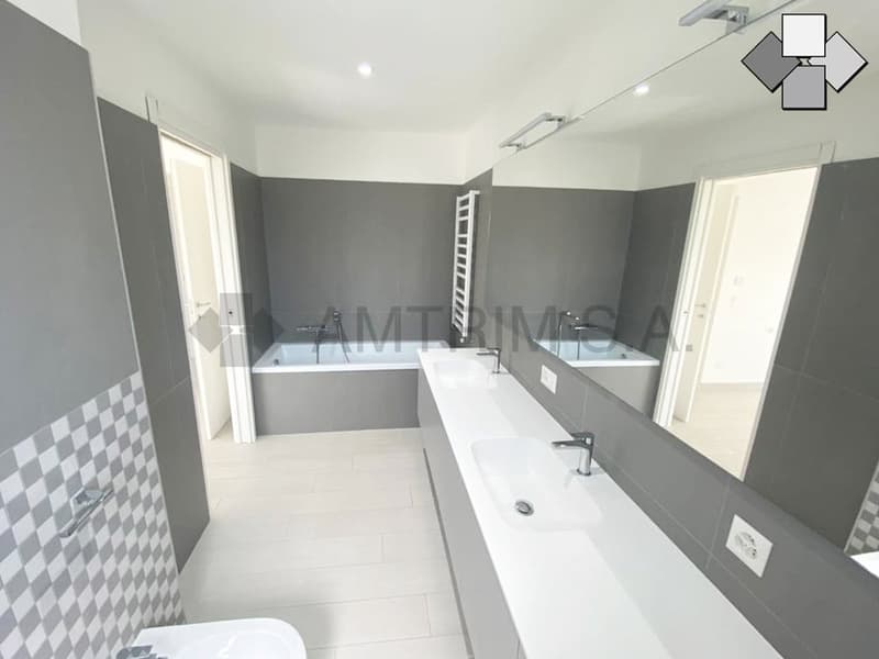 Large bathroom with grey walls, white tiles, two sinks, bathtub, and shower area