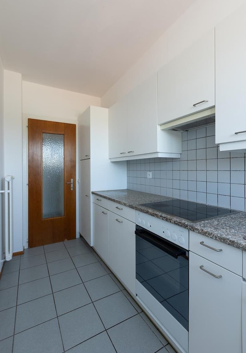 modern white kitchen with marble counter, wooden door, tile floor, built-in oven, stovetop