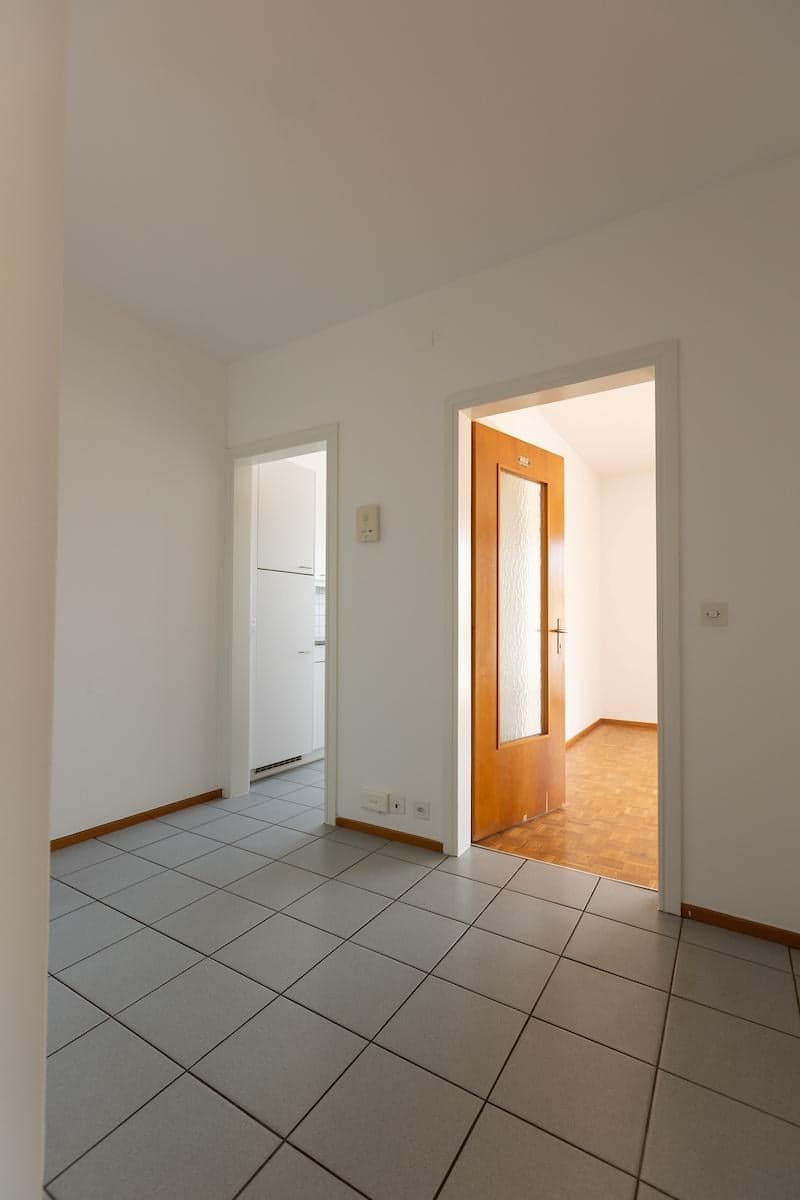 empty room, white walls, tiled floor, two doors, electric outlets, wooden floor in hallway