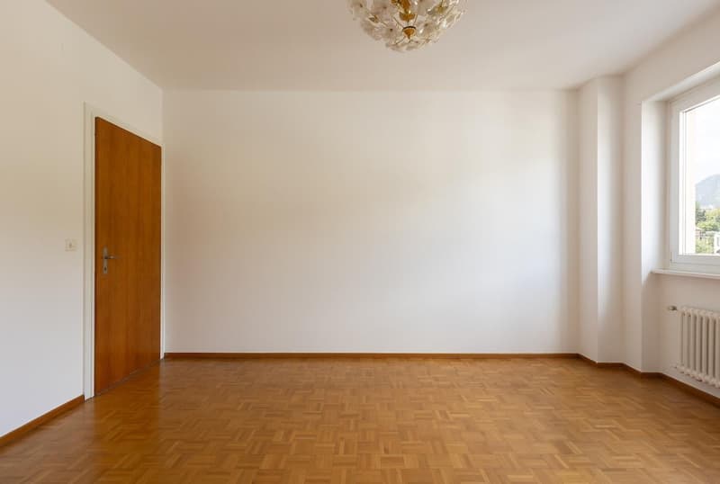 empty room, wooden parquet floor, white walls, wooden door, ceiling chandelier, window with view