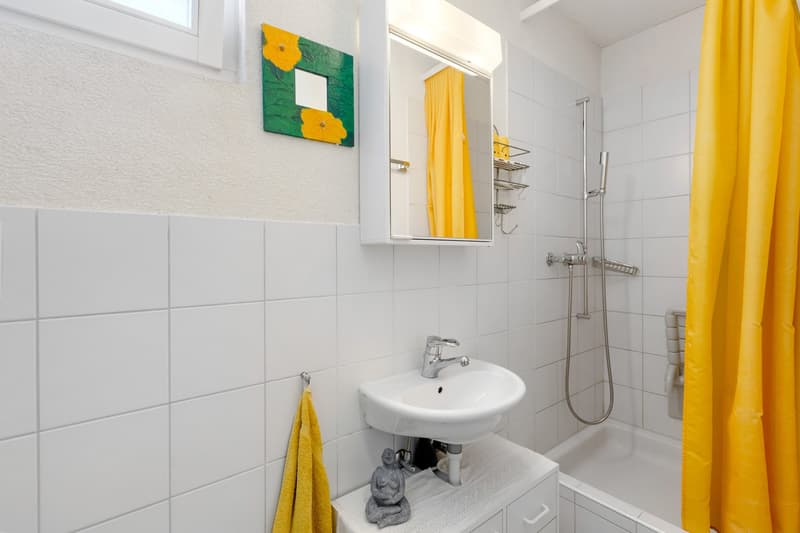 white tiled walls, white sink, mirror, shower, bathtub, yellow shower curtain, towel, sculpture