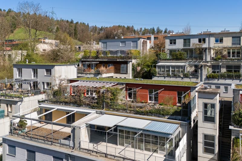 Multiple story building, green roofs, balconies, glass windows, metal railings, surrounded by trees and plants