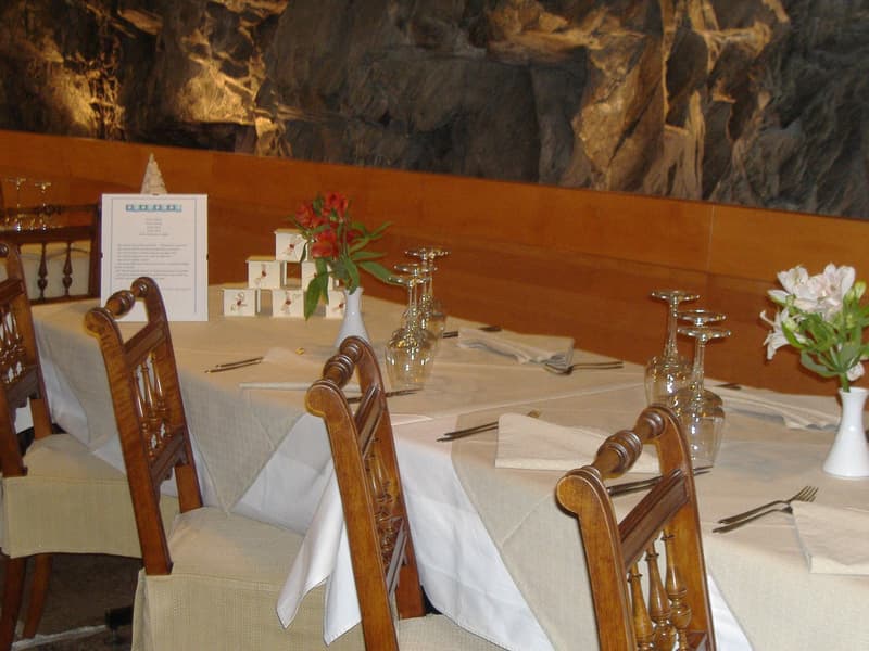 Dining room with wooden chairs, white tablecloth, flower vases, cutlery, and a menu card.
