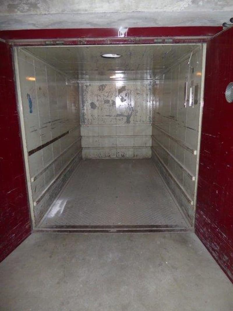 The image shows the interior of an elevator. The walls are tiled, and the floor is concrete. The elevator appears to be in a commercial or industrial building.