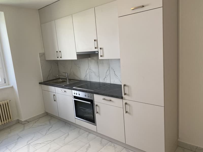 Modern, minimalist kitchen with white cabinets, marble-patterned backsplash, built-in oven and dishwasher, and stainless steel sink