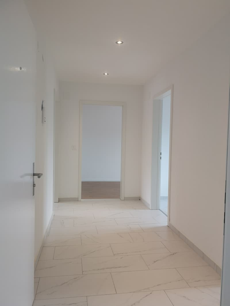 White tiled flooring, white walls, ceiling lights, doorways leading to other rooms, power outlet